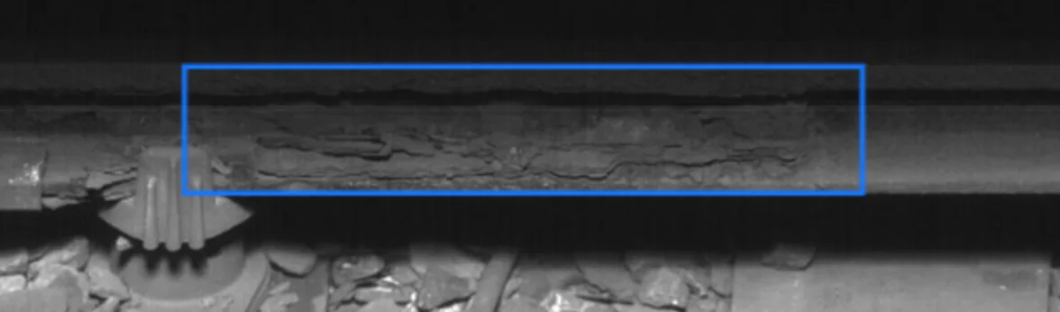 Line-scanning image of conductor rail showing a blue detection box highlighting an area of corrosion on the rail surface.