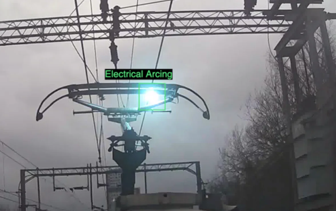 Upward-facing camera view of a pantograph with an electrical arcing event highlighted in a green detection box.