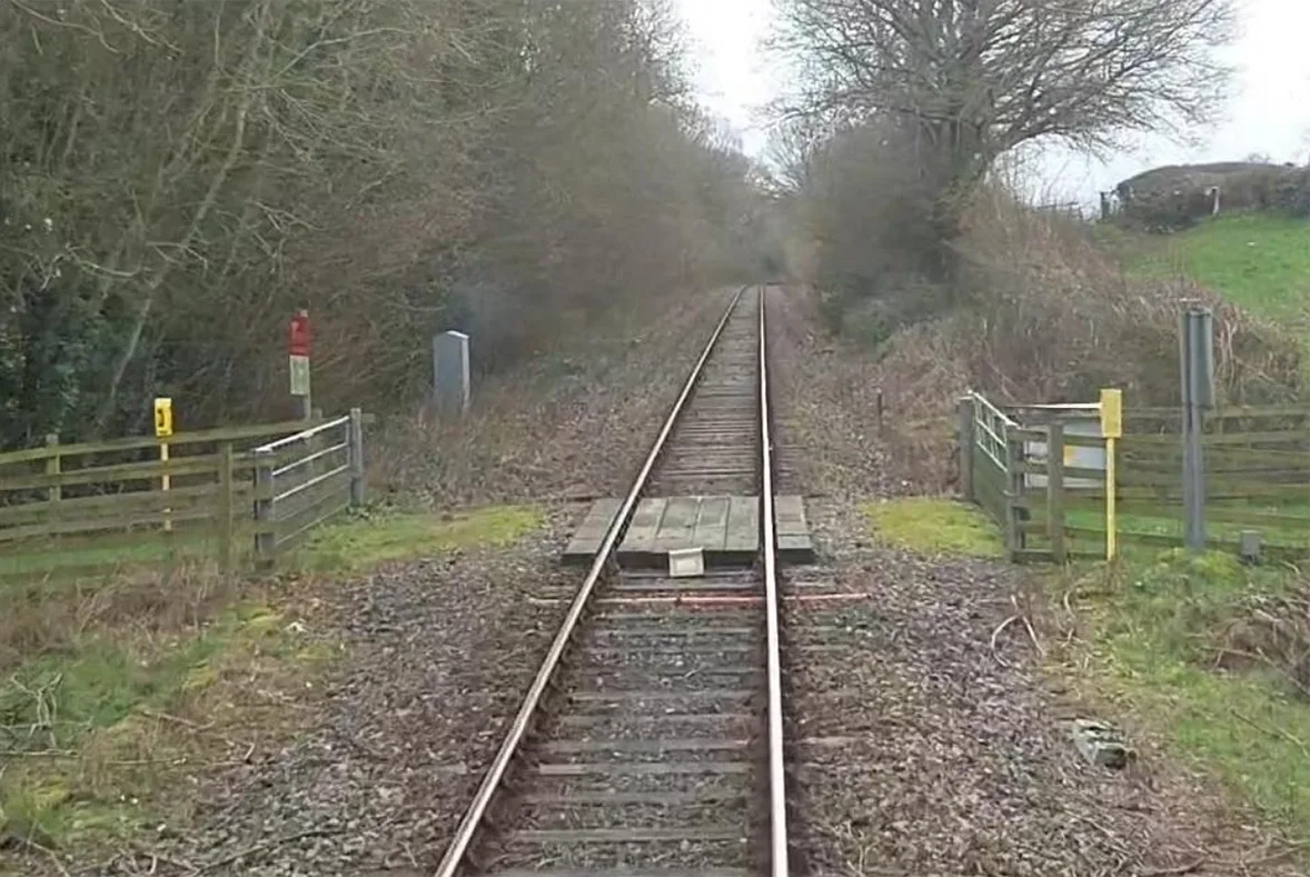 Forward-facing video showing a rural level crossing with gates, fencing, and warning signs visible on both sides of the track.