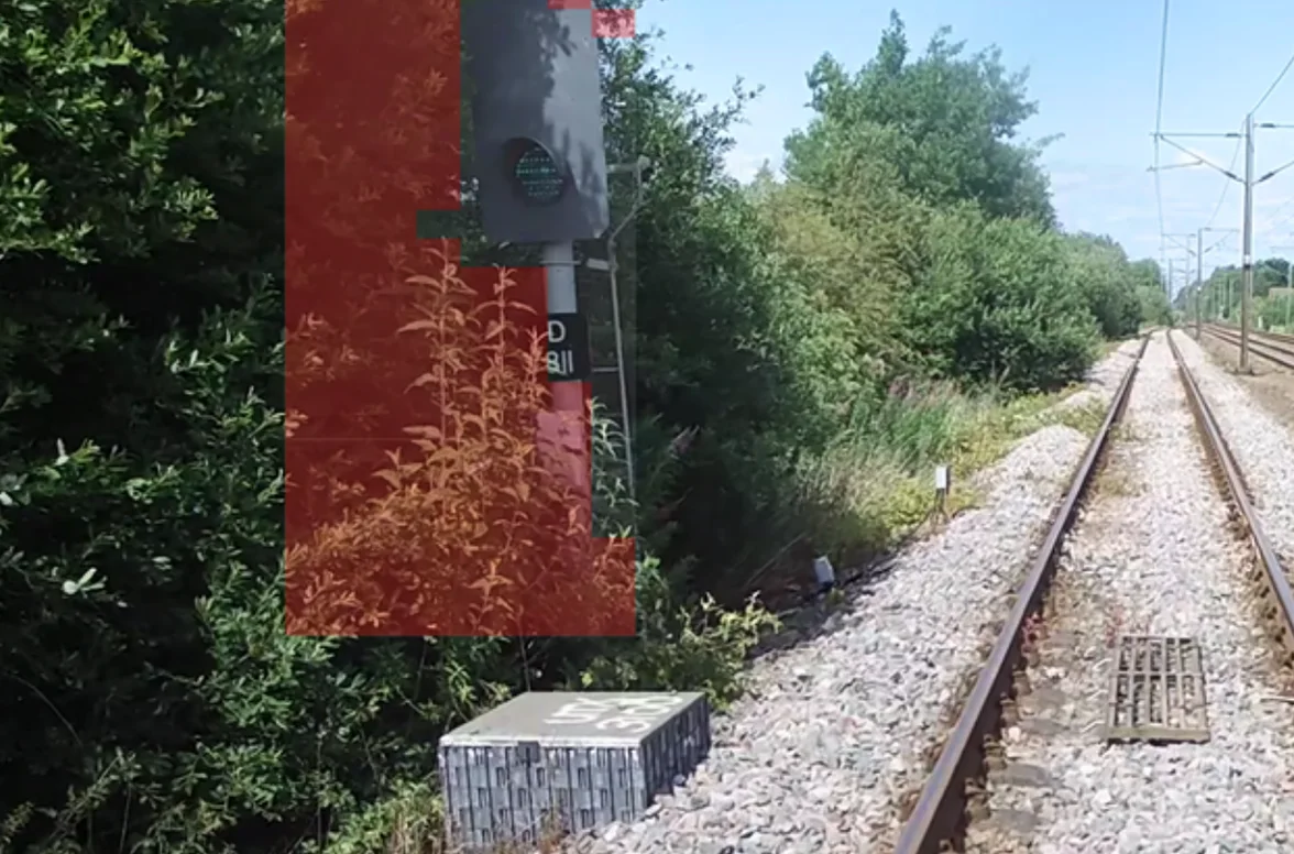 Forward-facing video showing a signal partially obscured by vegetation encroachment, with a red AI detection overlay highlighting the obstruction.