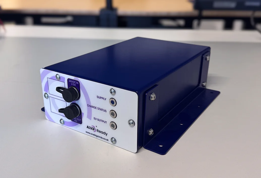 A navy blue AIVR Ready hardware unit with a white front panel showing 24VDC input and output ports, and three indicator lights labelled Supply, Charge Status and 5V Output.