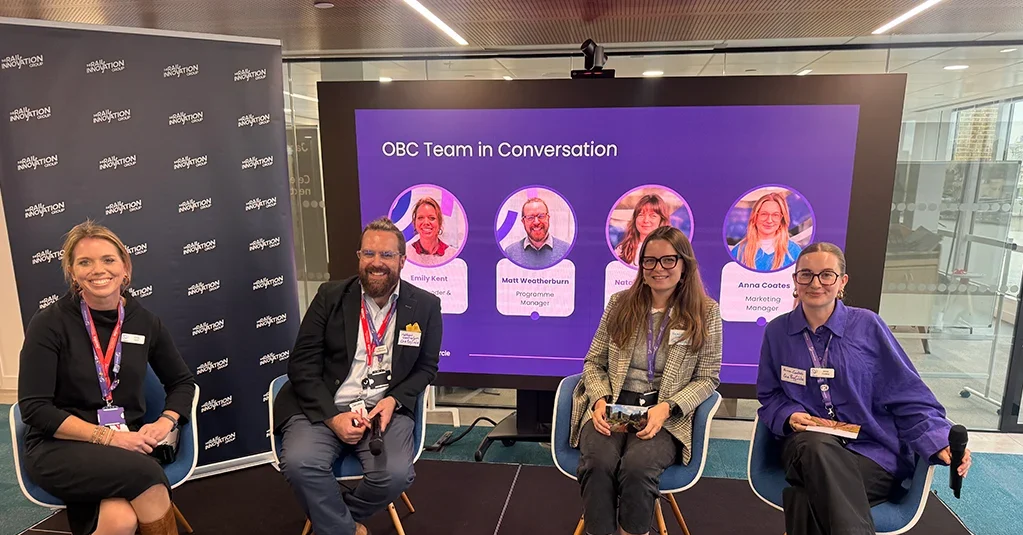 Four members of the OBC team seated on stage in front of a screen reading “OBC Team in Conversation”.